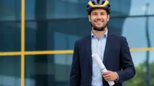Salarié cycliste souriant tenant son contrat de travail, casque vélo sur la tête, devant un immeuble de bureaux