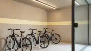 Local vélo d'entreprise fermé : arceaux alignés, vélos électriques bleu nuit attachés par le cadre, porte à badge et éclairage